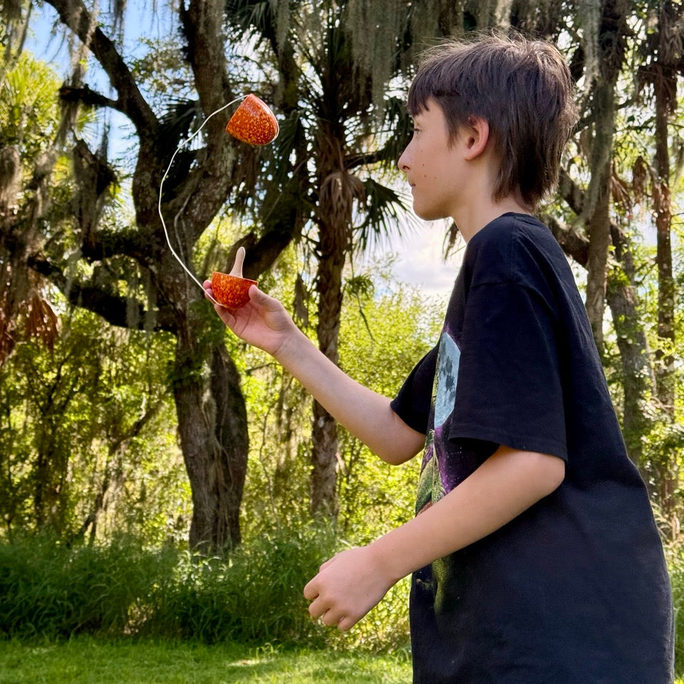 Boy wearing a black shirt, standing in a field, playing with a BK Egg that's orange. 